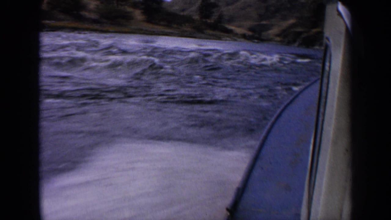 End frame of 1963 Idaho 8mm river travel, with the boat edge at right, turbulent water below, and rugged shoreline behind.