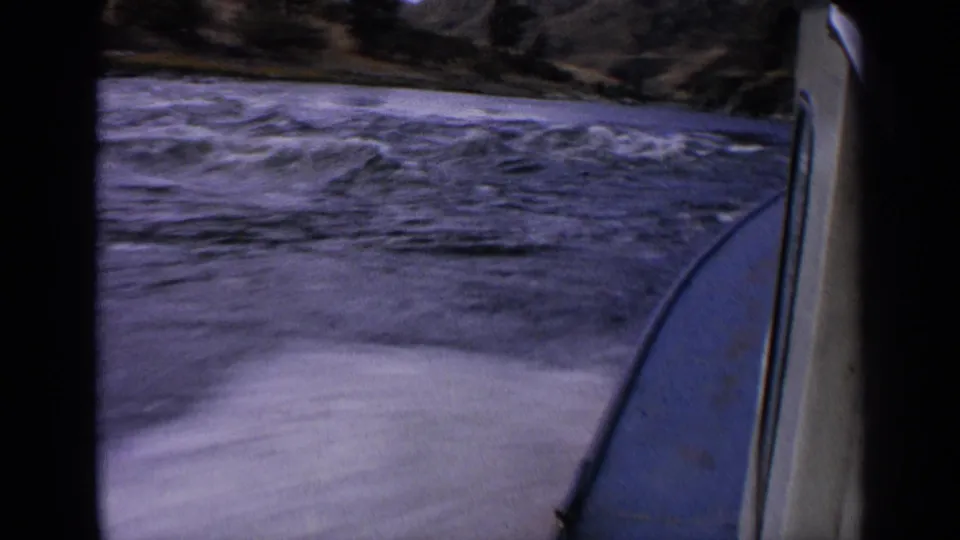 End frame of 1963 Idaho 8mm river travel, with the boat edge at right, turbulent water below, and rugged shoreline behind.