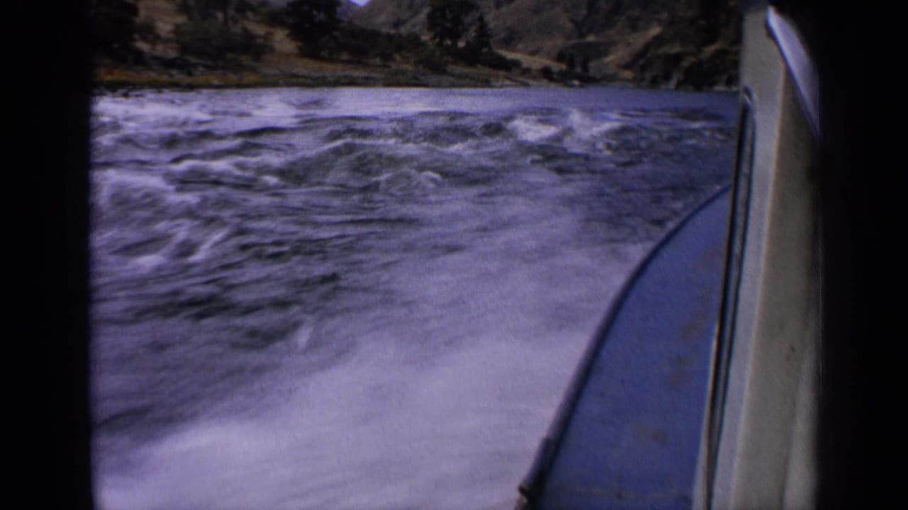 1963 Idaho 8mm frame from a moving motorboat, showing the bow at right and turbulent river water ahead.