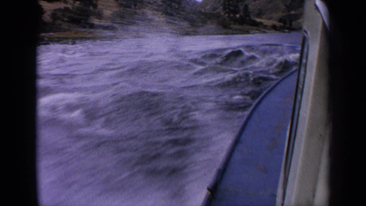 First-person 8mm view from a motorboat on an Idaho river, with swirling water and shoreline visible ahead.