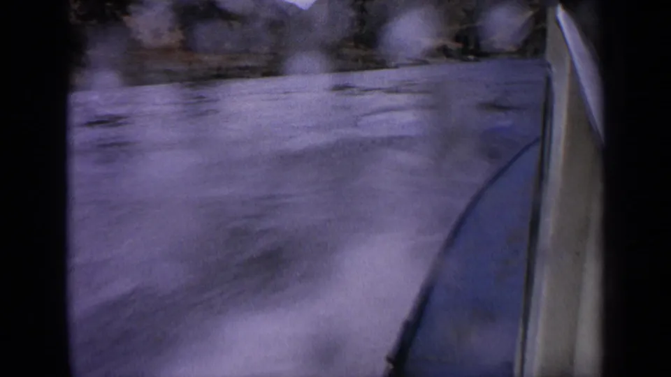 1963 Idaho home-movie frame showing a boat edge, blurred water, spray, and rocky canyon terrain in the distance.