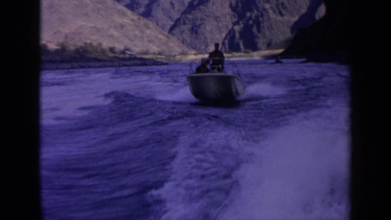 1963 Idaho 8mm frame with a small motorboat carrying a distant person across a wake in a steep canyon river setting.