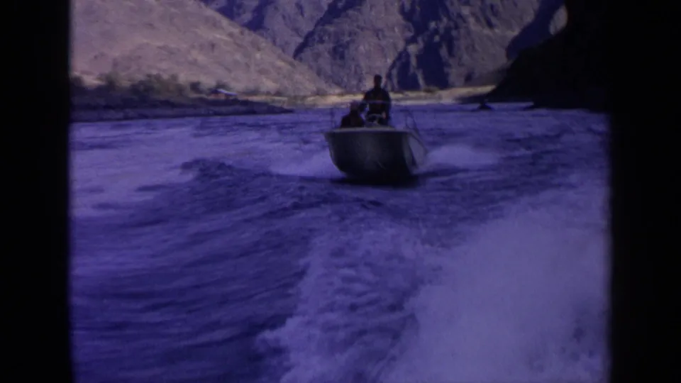 1963 Idaho 8mm frame with a small motorboat carrying a distant person across a wake in a steep canyon river setting.