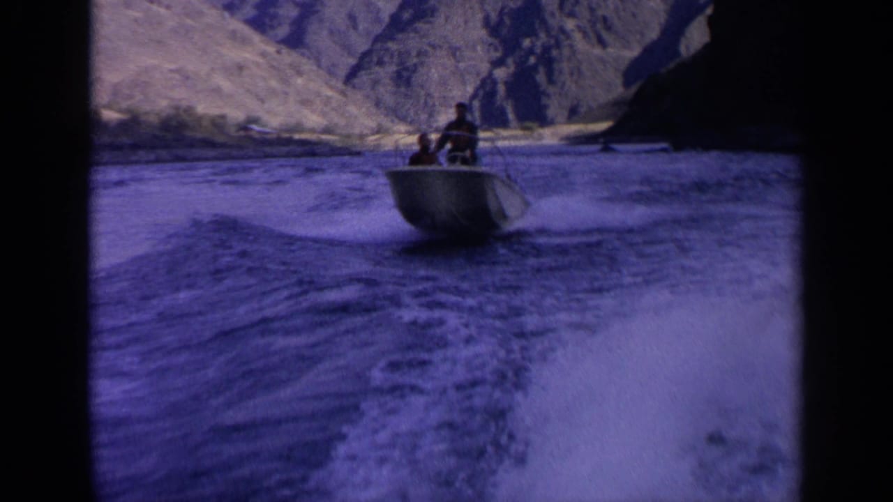 Small motorboat with two men speeding on a river between rocky canyon slopes.