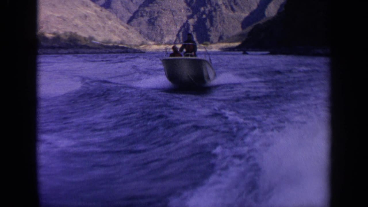 Blue-purple 8mm frame of two men in a small motorboat traveling through a rocky Idaho canyon river.