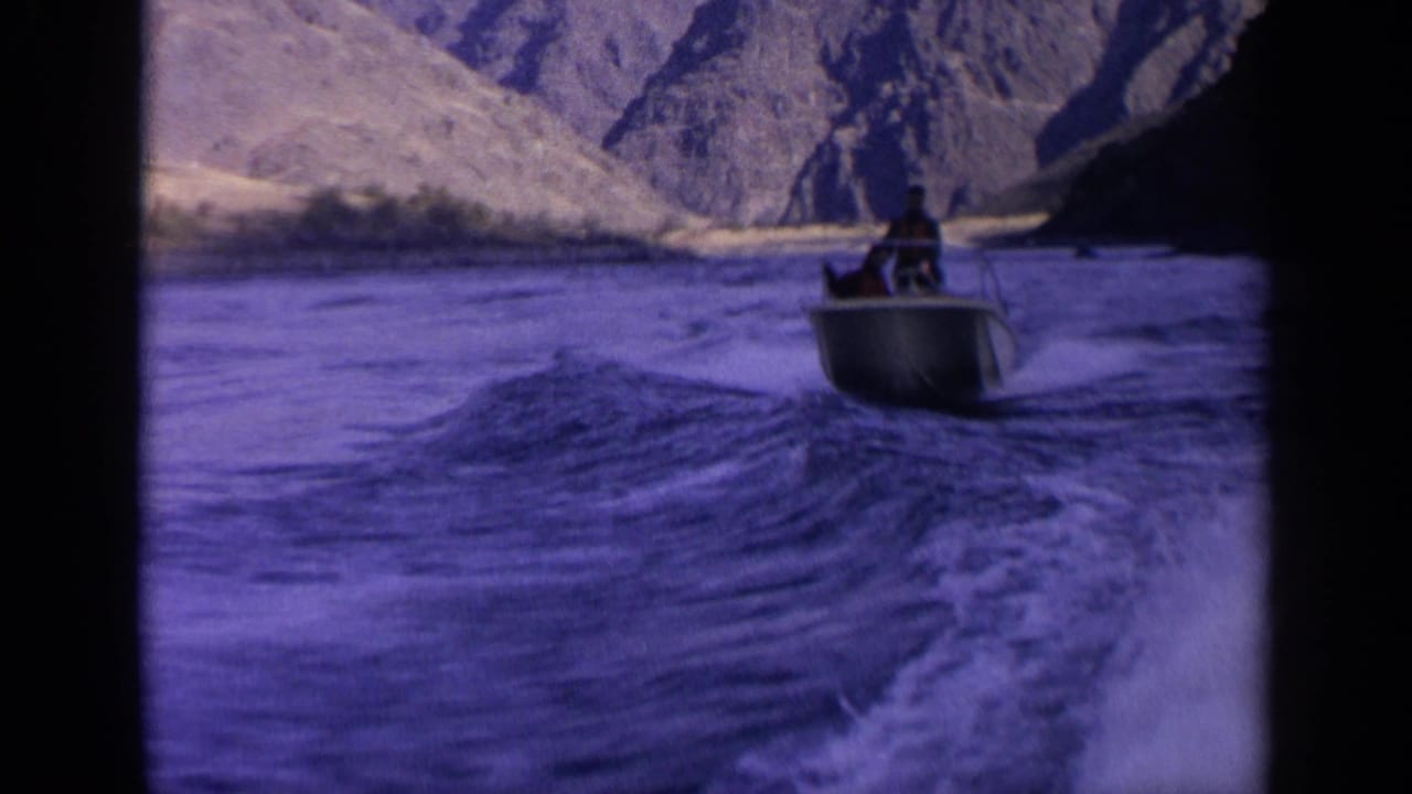 Small motorboat ahead on rough river water between arid mountain slopes.