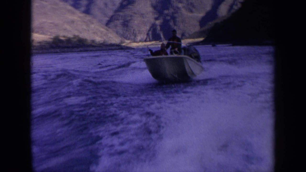 Close home-movie view of a sturdy motorboat with passengers riding over rough river water in Idaho mountain terrain.