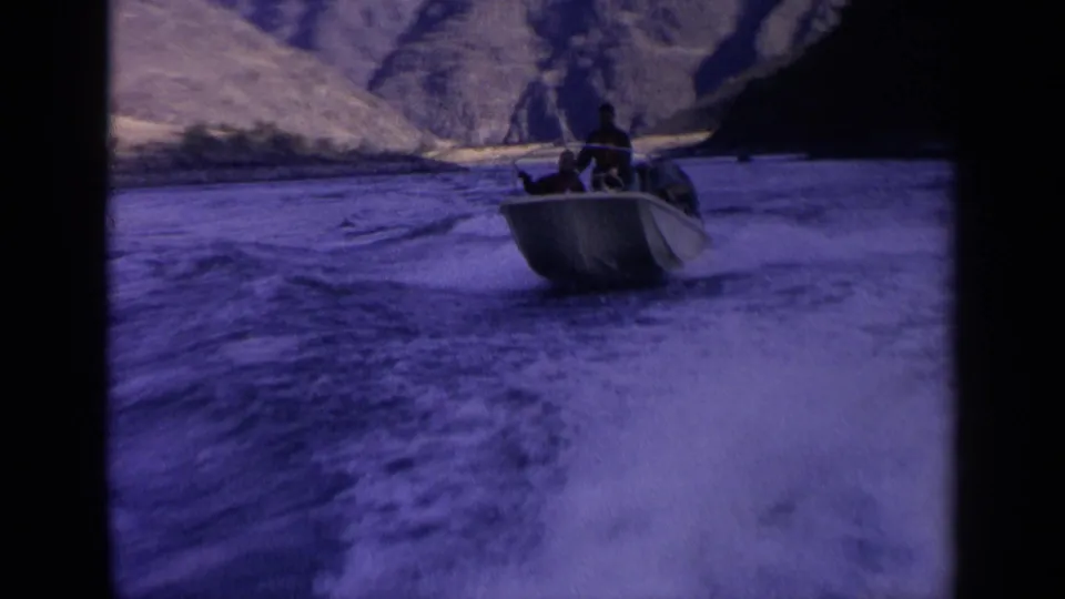 Close home-movie view of a sturdy motorboat with passengers riding over rough river water in Idaho mountain terrain.
