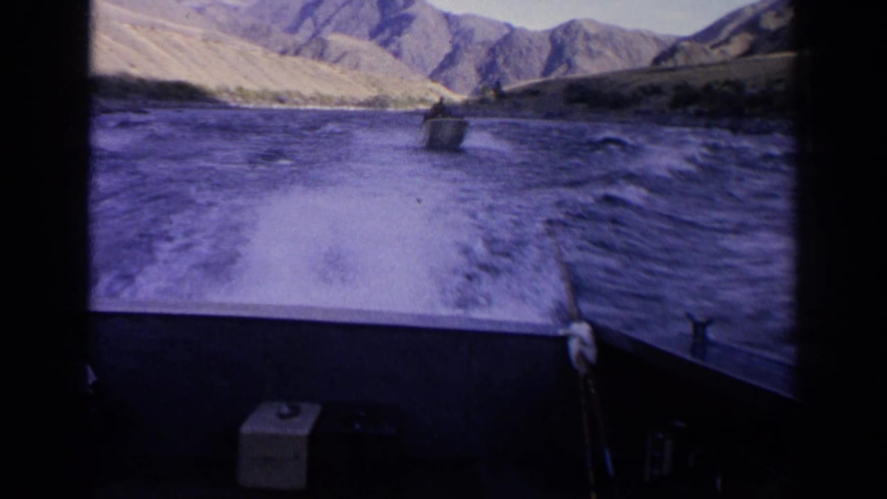 View from the stern area of one boat toward another motorboat ahead on choppy Idaho river water amid rugged mountain scenery.