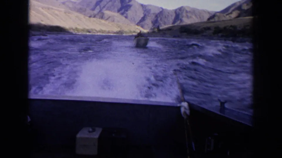 View from the stern area of one boat toward another motorboat ahead on choppy Idaho river water amid rugged mountain scenery.
