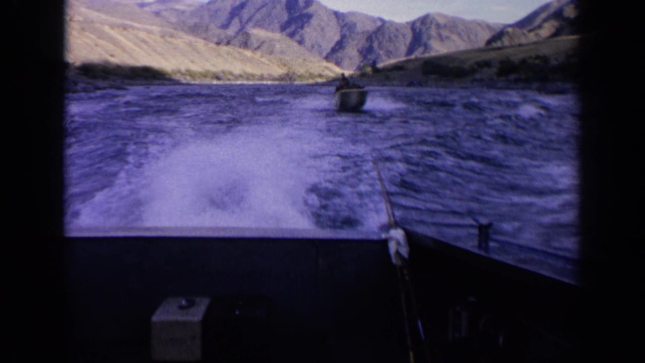 Boat wake on a wide river with a small boat ahead and mountains in the background.
