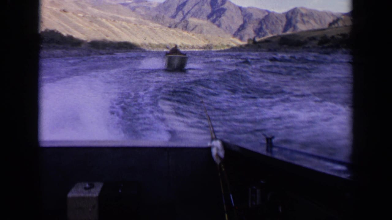 1963 Idaho 8mm frame from a moving boat, showing a foamy wake, another small boat ahead, and arid mountains beyond the river.
