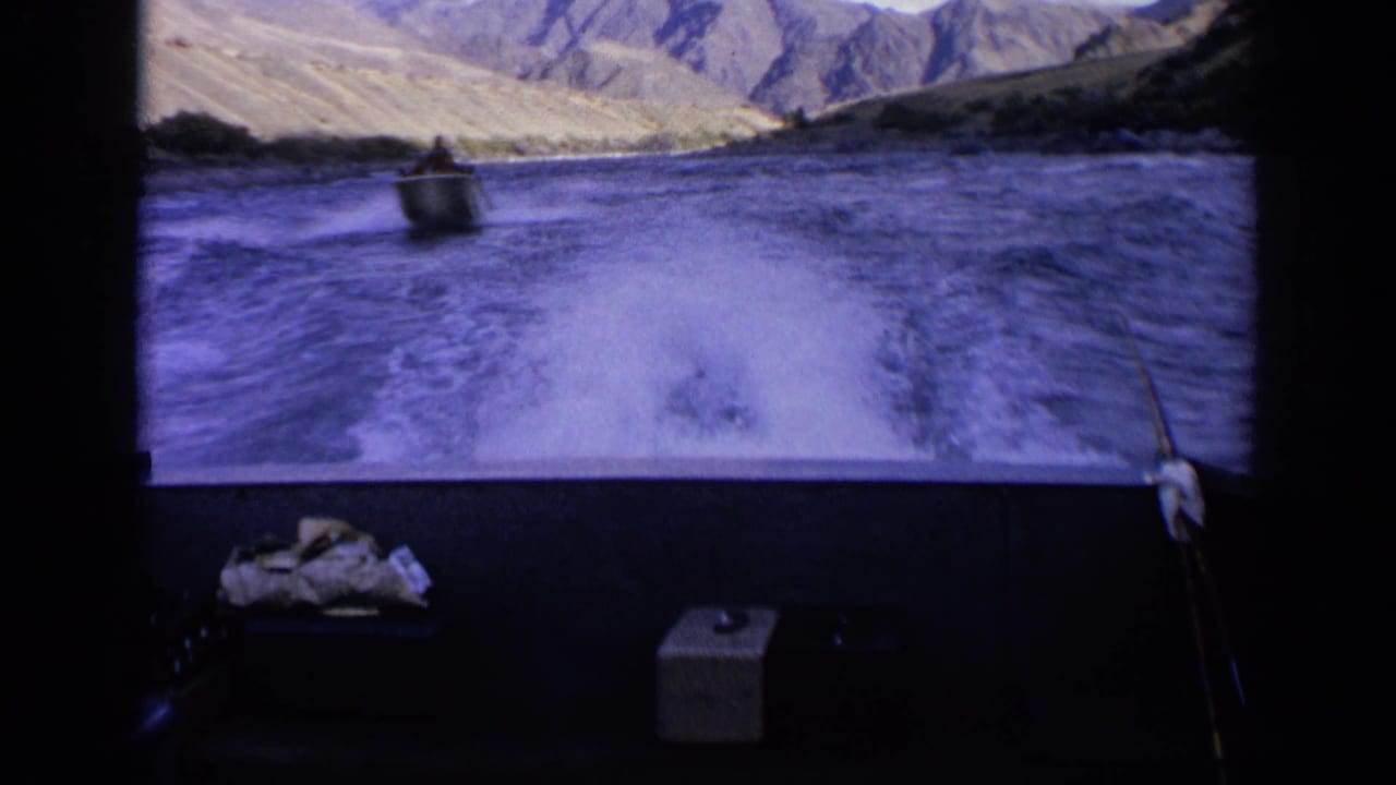 1963 Idaho boating view with a small motorboat ahead, foamy wake in the foreground, and dry hills around the lake.