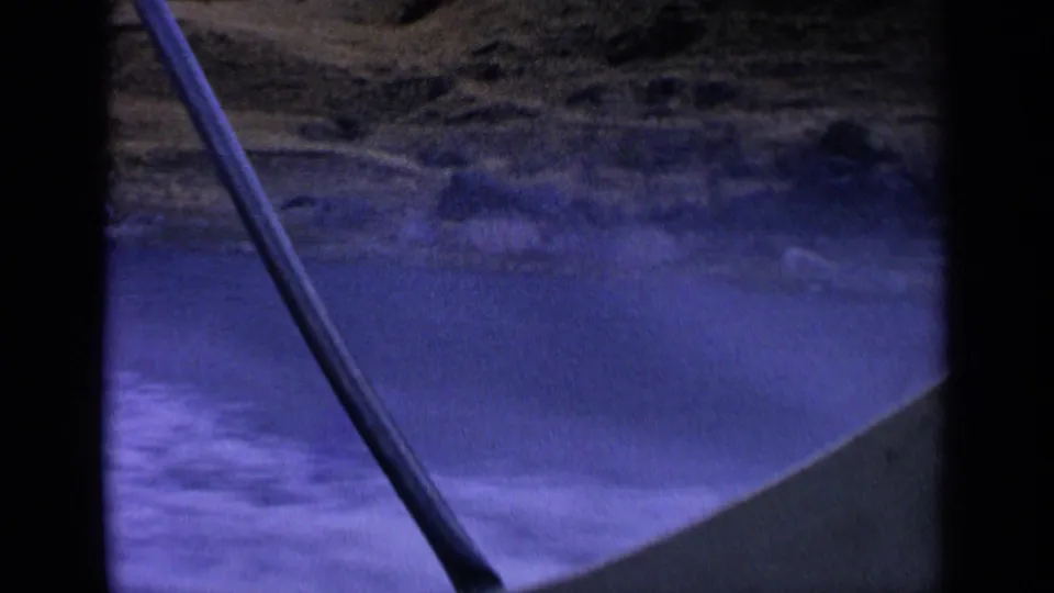 Handheld 8mm view from inside a boat on an Idaho desert lake, with wake, shoreline, and a fishing rod crossing the frame.