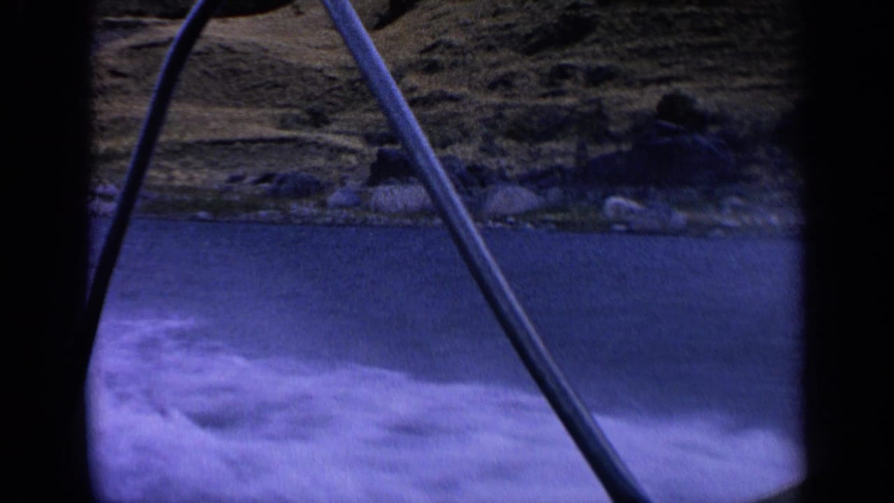 1963 Idaho home-movie frame from a moving boat, showing a fishing rod, foamy water, and dry shoreline along the lake.