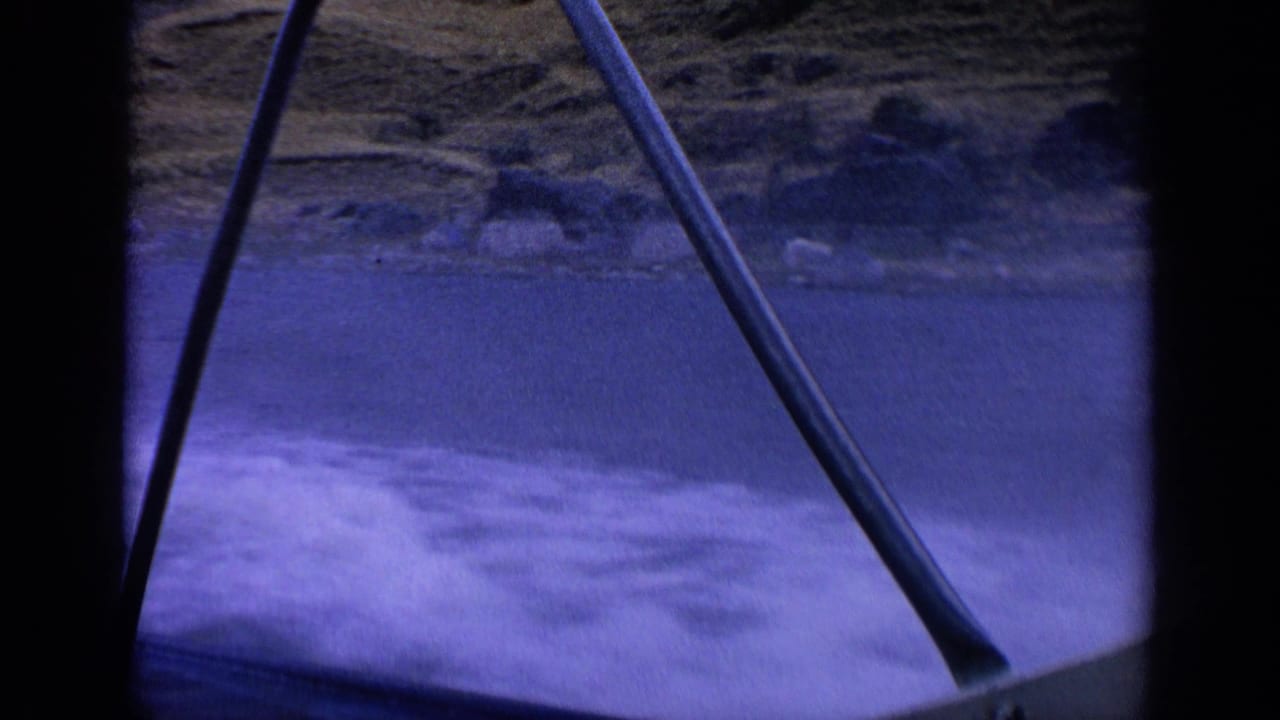 Boat railings frame blue water and white wake near a rocky shoreline.
