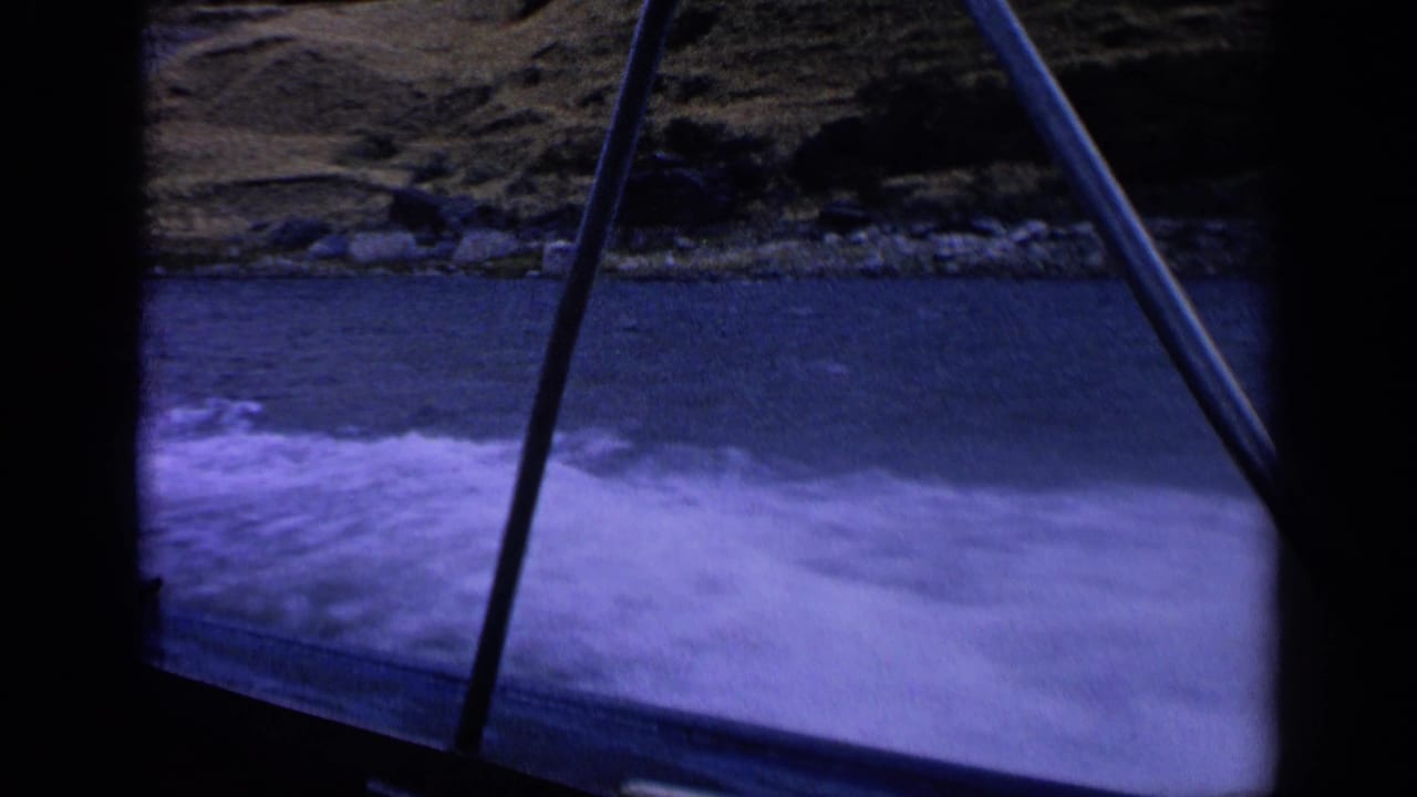 Boat wake churns across a mountain lake, framed by dark parts of the vessel.