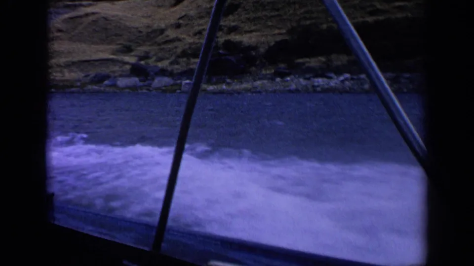 1963 Idaho 8mm frame showing foamy boat wake on a mountain lake, with shoreline and boat structure partly blocking the view.