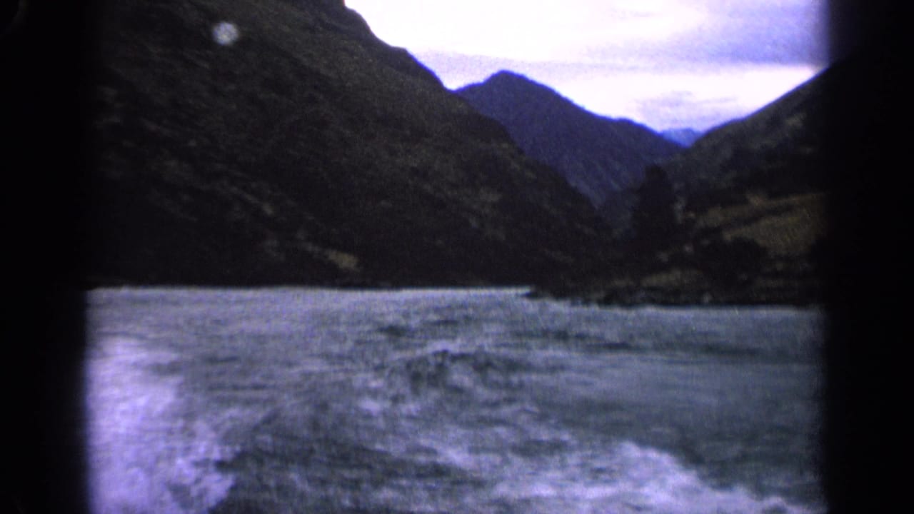 1963 Idaho 8mm view of a moving boat wake stretching across a mountain lake beneath an overcast sky.