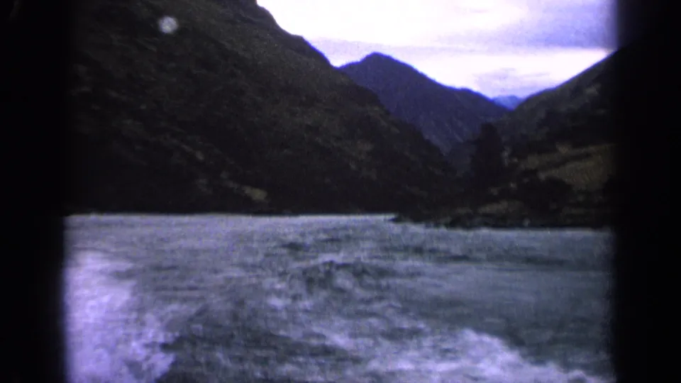 1963 Idaho 8mm view of a moving boat wake stretching across a mountain lake beneath an overcast sky.