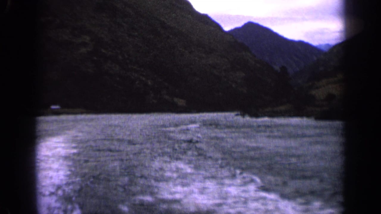 Choppy mountain lake seen from a moving boat with a foaming wake and dark slopes ahead.