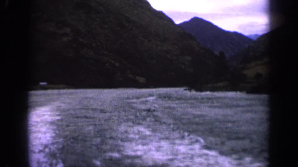 1963 Idaho 8mm frame showing a boat wake across choppy lake water between dark mountain slopes under a cloudy sky.