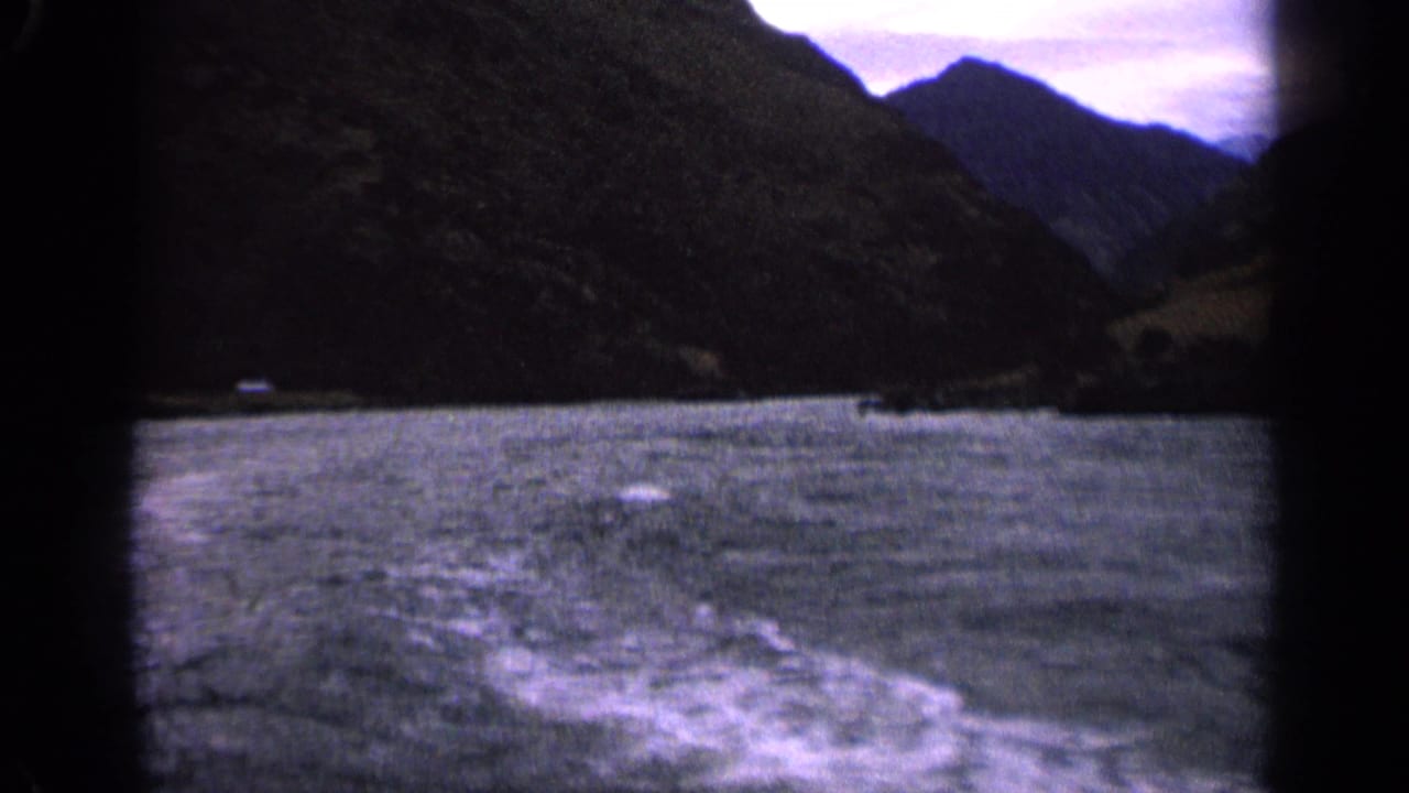 1963 Idaho home-movie frame of rough lake water and a trailing boat wake, with steep mountain slopes on both sides.