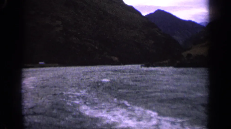 1963 Idaho home-movie frame of rough lake water and a trailing boat wake, with steep mountain slopes on both sides.