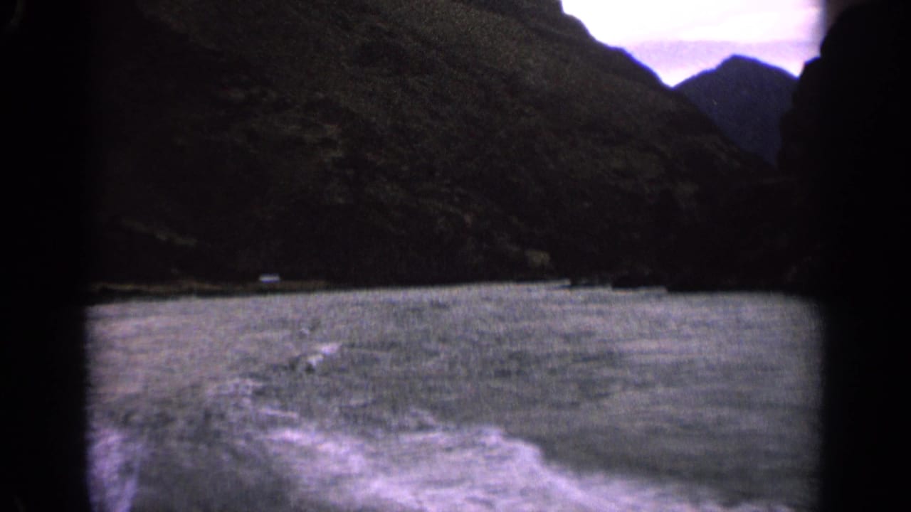 Boat wake on a lake between dark mountain slopes with pale sky above.