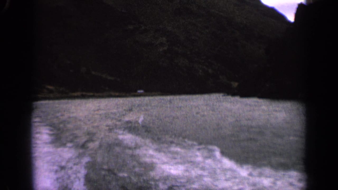 1963 Idaho 8mm view from a boat, with foamy wake in the foreground and dark lakeside hills beyond.
