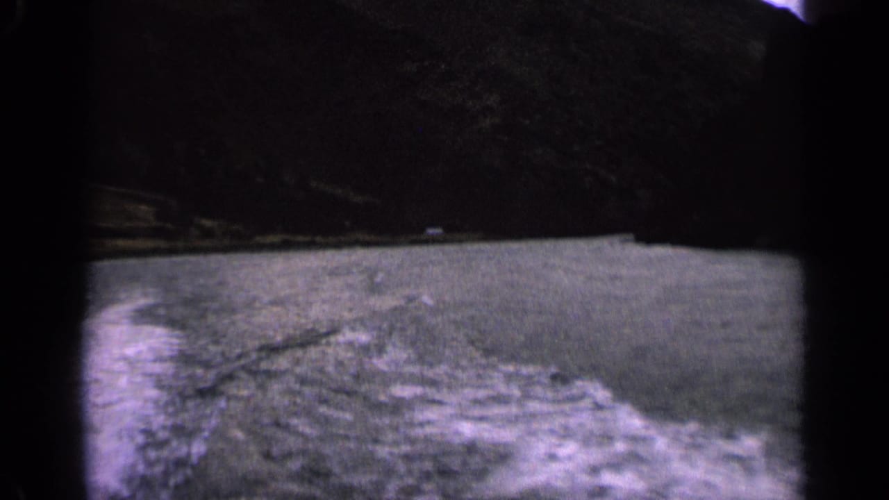 1963 Idaho home-movie frame with choppy lake water, a low shoreline, and dark mountains seen from a moving boat.