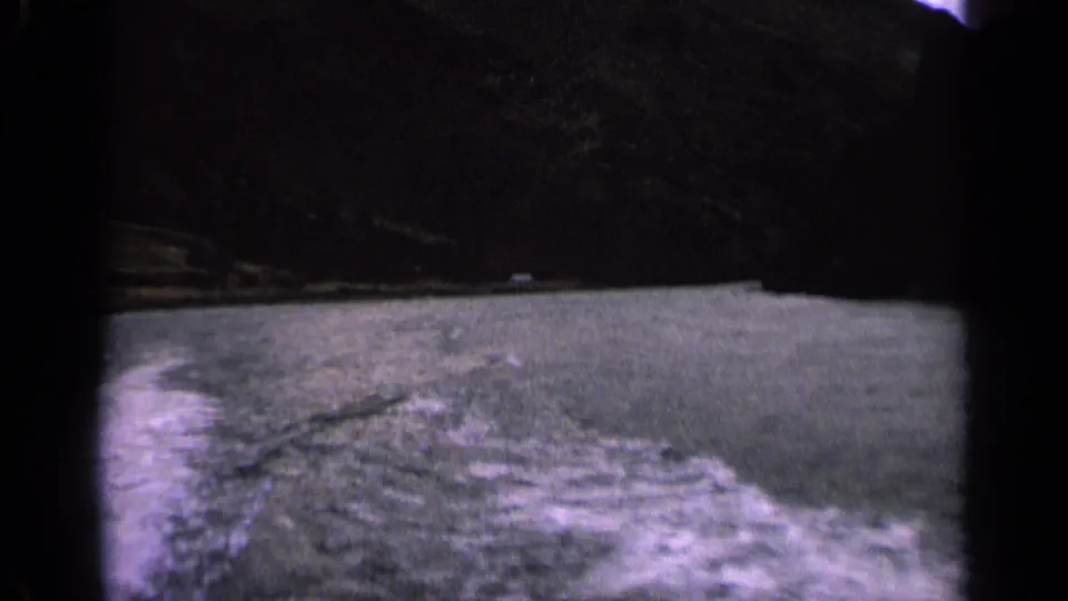 1963 Idaho home-movie frame with choppy lake water, a low shoreline, and dark mountains seen from a moving boat.