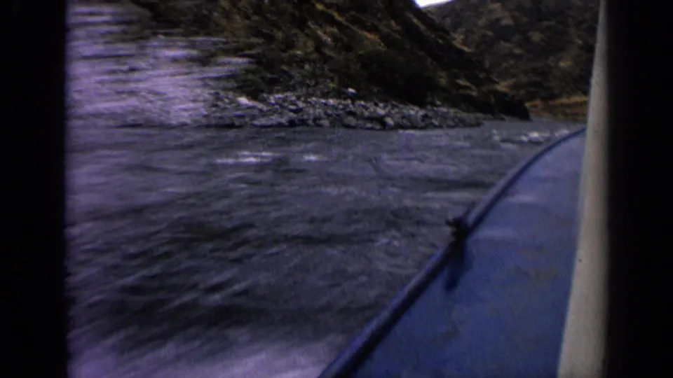 Final 1963 Idaho 8mm frame showing a boat rail, wake in the foreground, and rocky riverbanks ahead.