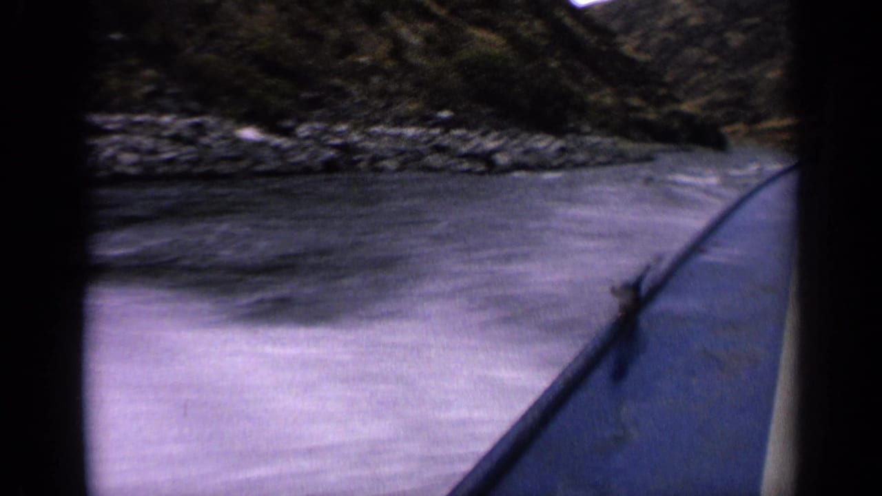 Forward view from a boat along a rocky river with dark film borders.