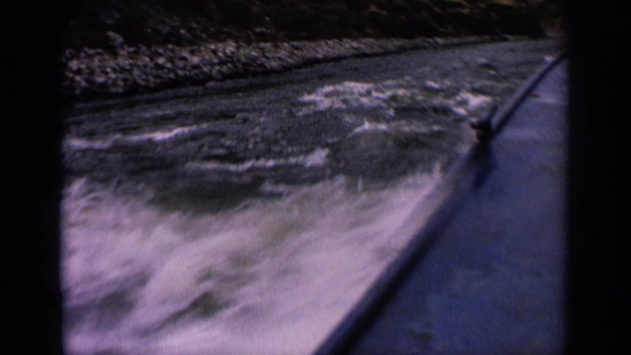 Boat bow cutting through rough lake water near a rocky mountain shoreline.