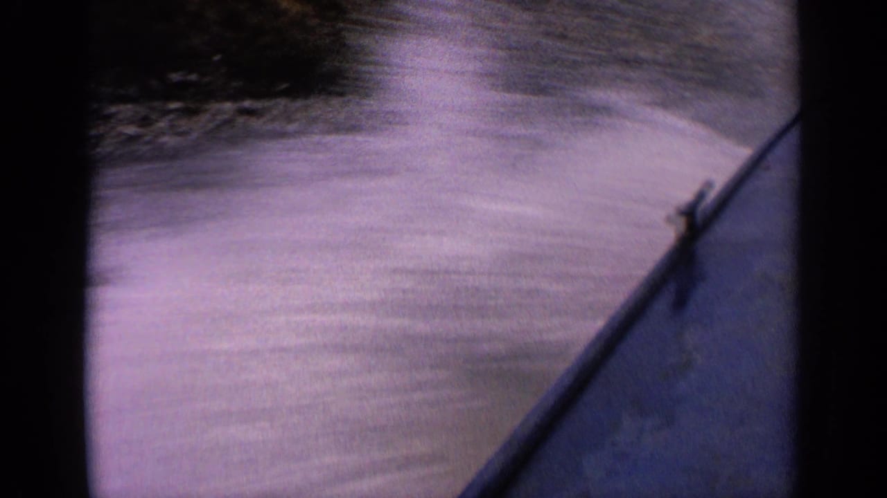 Purple-tinted 8mm frame showing the boat bow and foamy wake across an Idaho mountain lake.