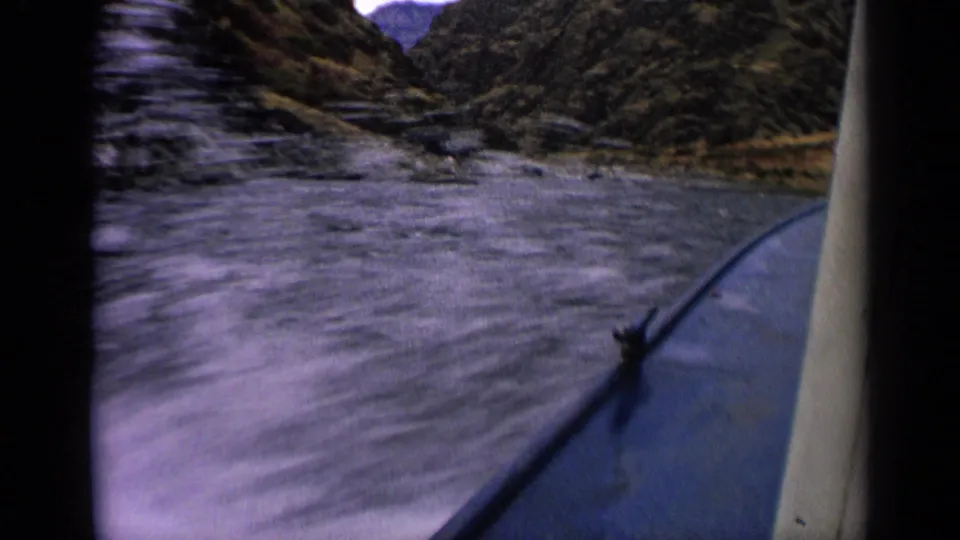 1963 Idaho 8mm view from inside a boat moving through a narrow river with rocky canyon slopes ahead.