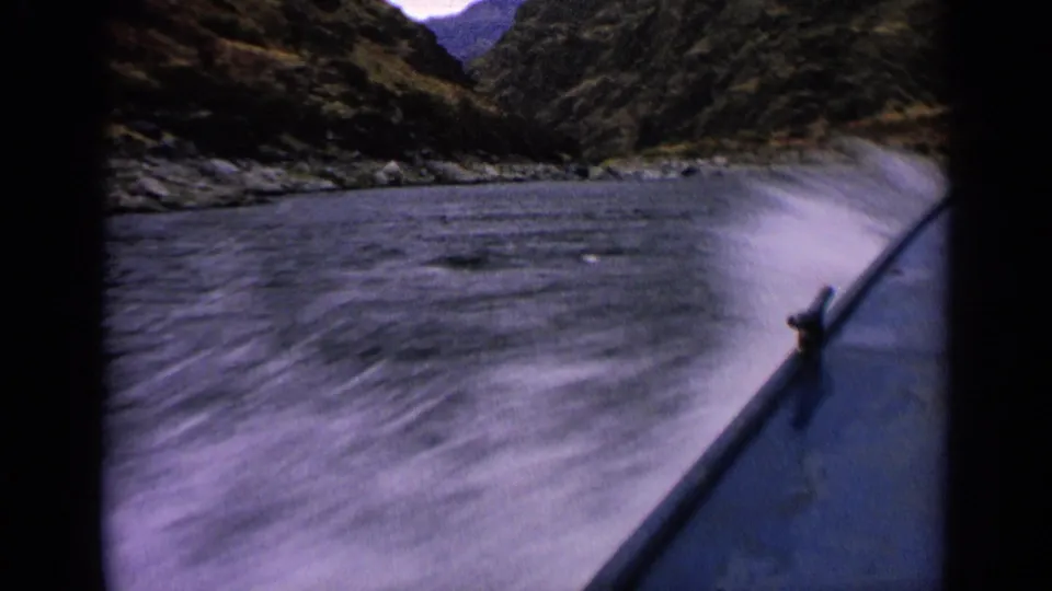 1963 Idaho home-movie frame showing the boat bow kicking up white spray in a rocky river channel.