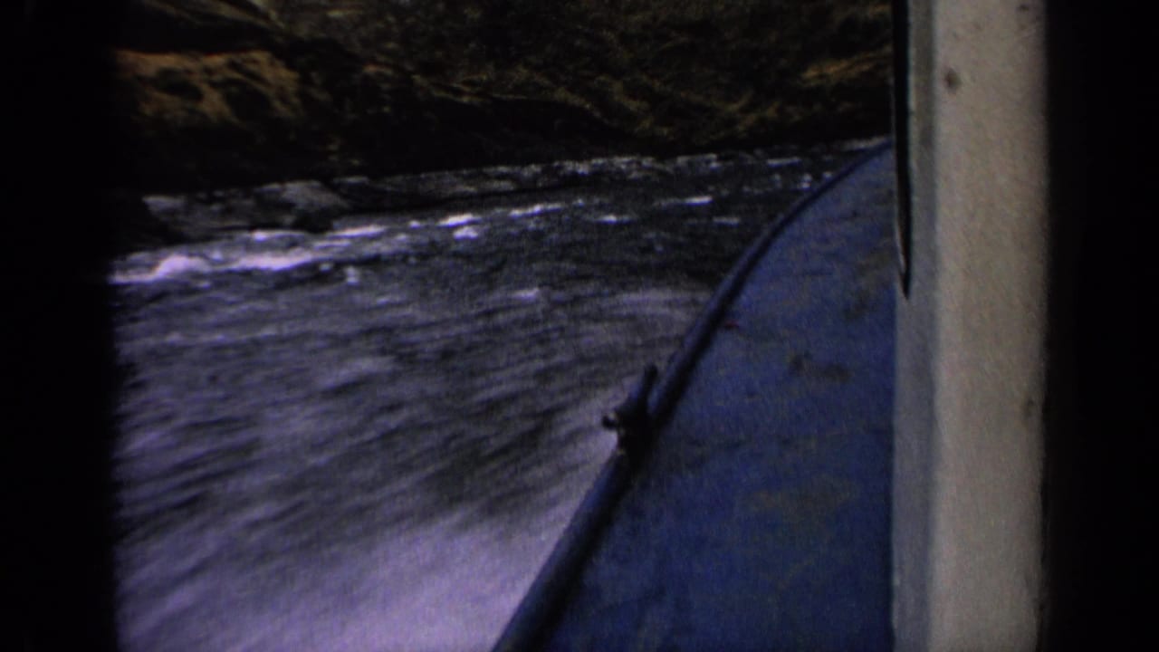 Final 1963 Idaho river-boating frame with the bow at right and choppy water passing rocky canyon banks.