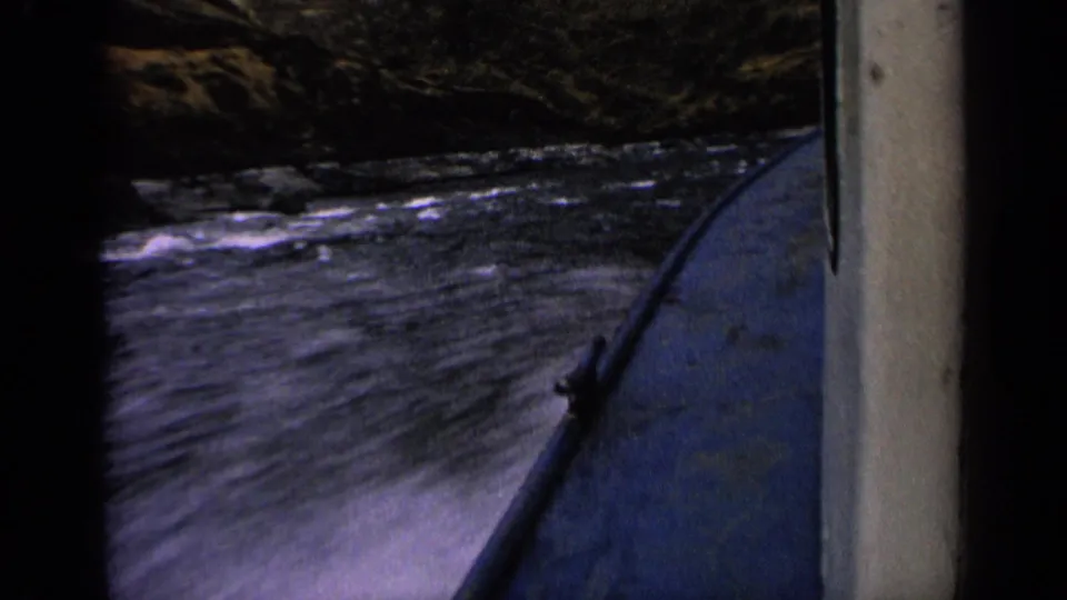 Final 1963 Idaho river-boating frame with the bow at right and choppy water passing rocky canyon banks.