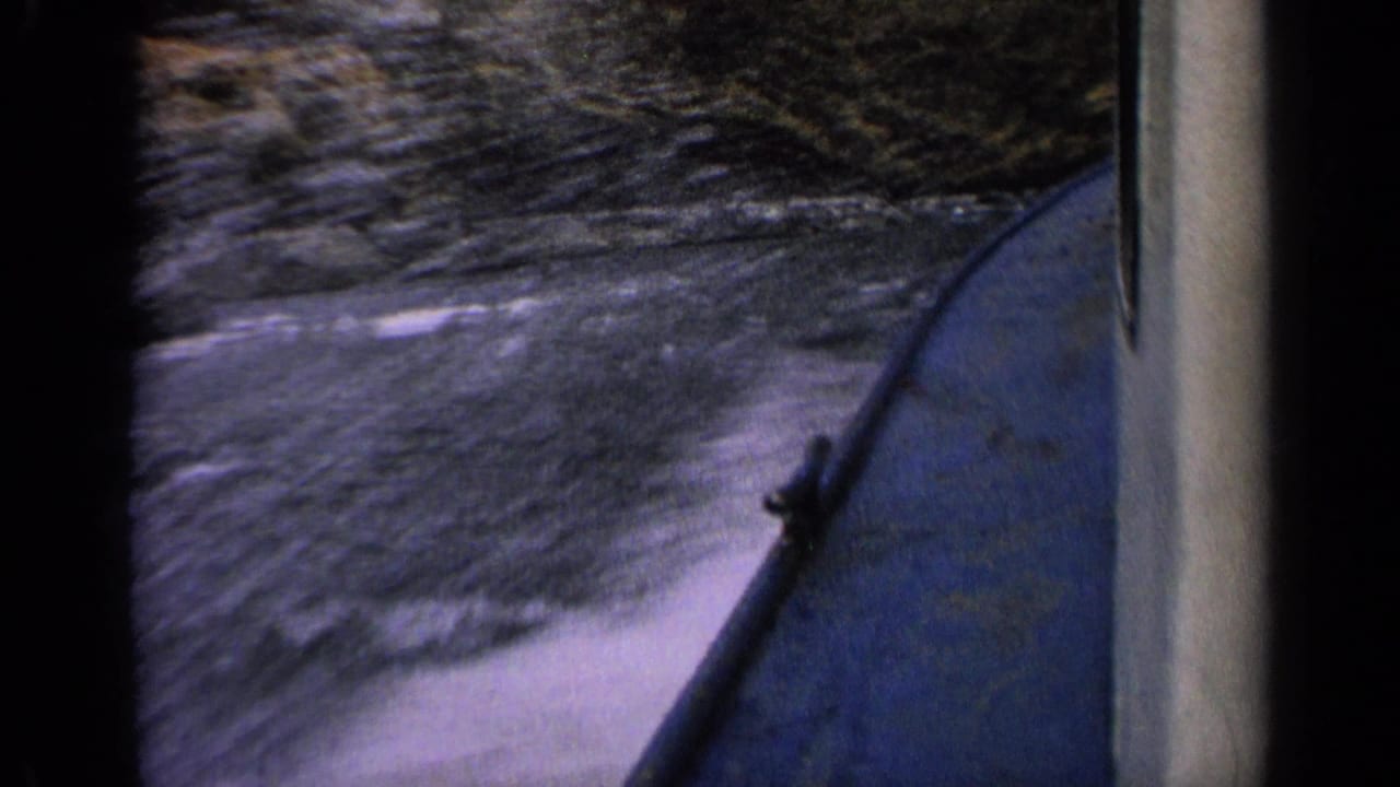 Boat hull at right with blurred water wake and rocky riverbank beyond.