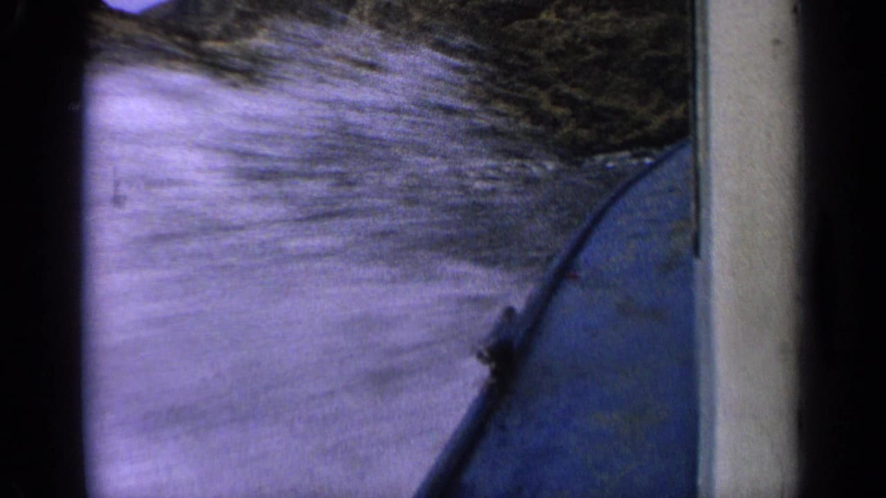 Blue boat hull cutting through blurred river water beside a dark bank.