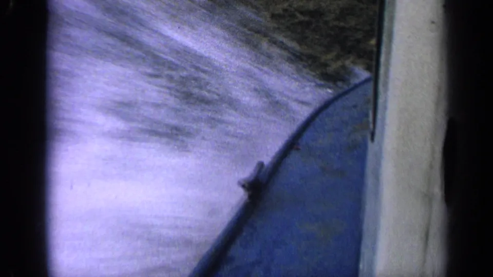 1963 Idaho home-movie frame with blue boat hull at right and bright, motion-blurred water splashing alongside.