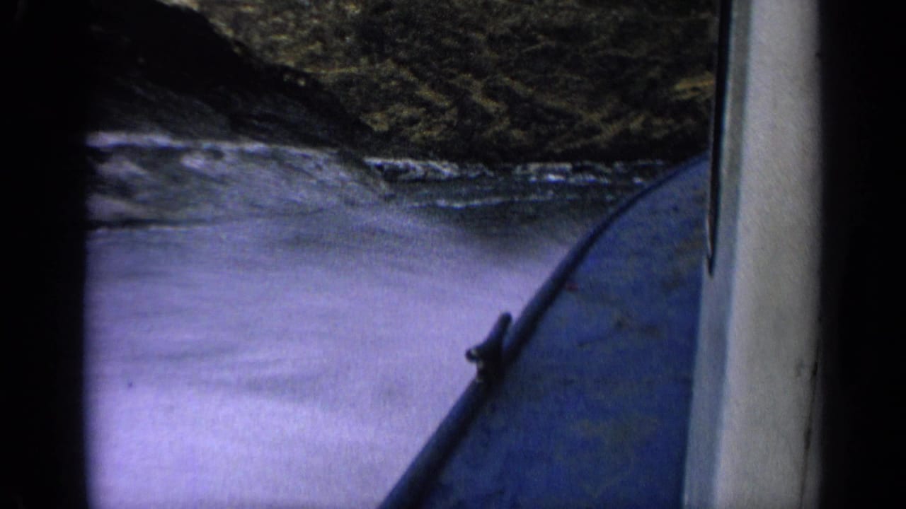 Blue boat bow cutting through choppy water beside dark canyon rock.