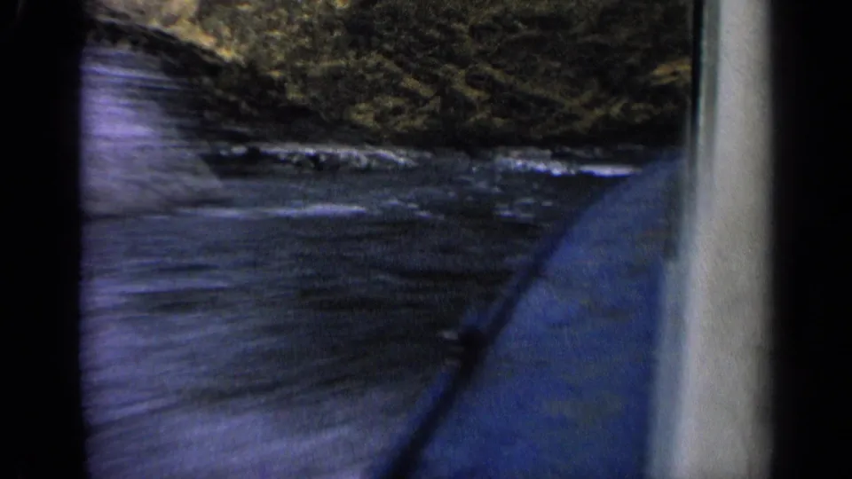 1963 Idaho home-movie view from a blue boat passing through rippled water with canyon rock close ahead.