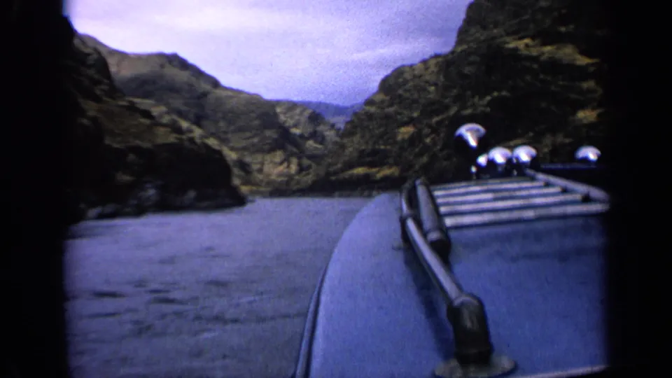 1963 Idaho 8mm frame showing a blue boat deck and silver horn as the river opens toward rocky mountains.