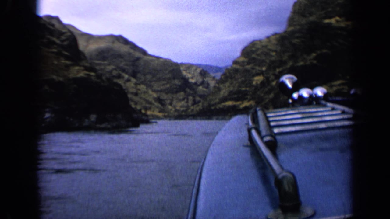 The moving boat’s bow appears at frame right while calm water leads between dark rocky canyon walls in this 1963 8mm footage.