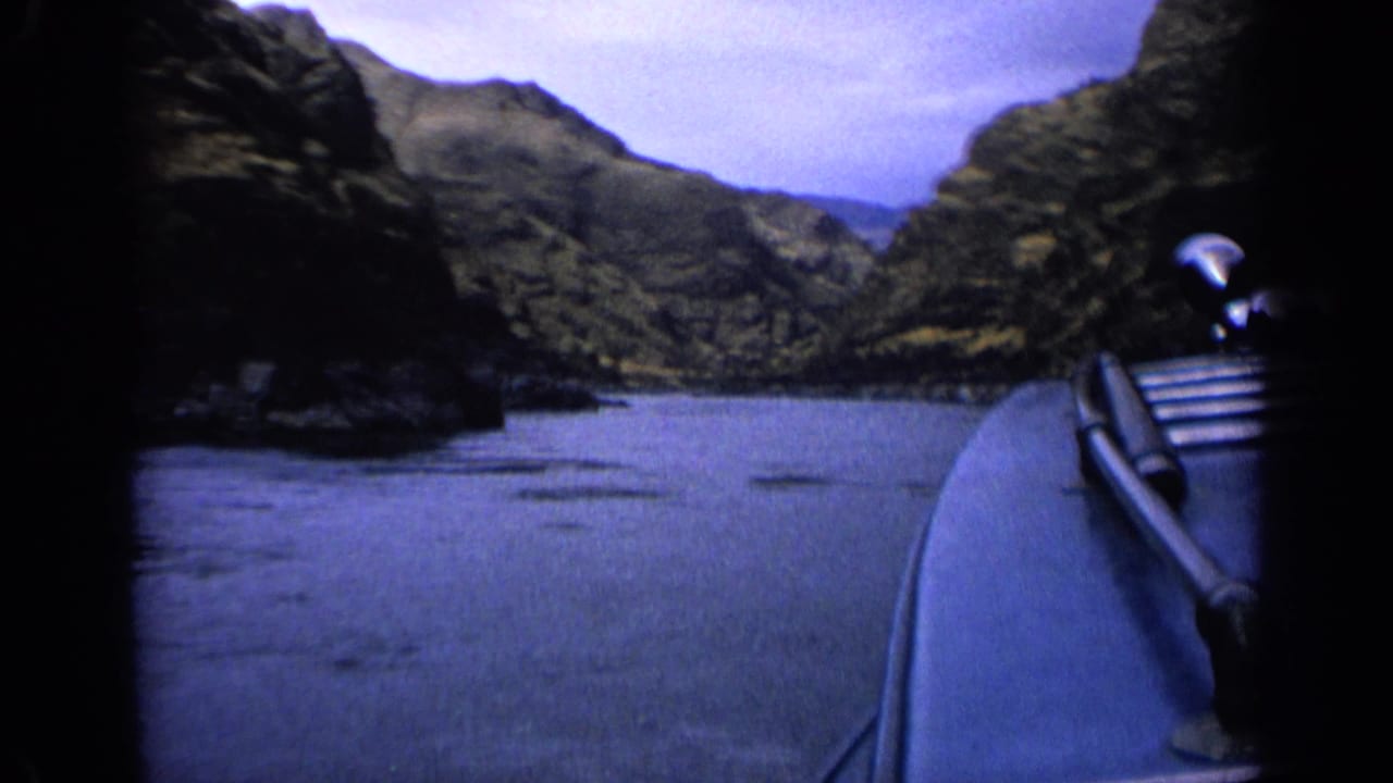 The boat’s right edge and rail pass through the frame as the canyon waterway opens ahead under a pale cloudy sky.