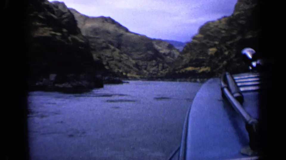 The boat’s right edge and rail pass through the frame as the canyon waterway opens ahead under a pale cloudy sky.