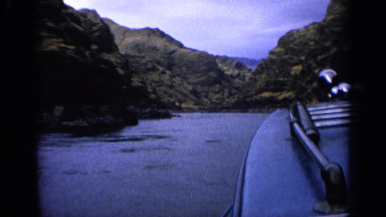 1963 Idaho 8mm frame showing a first-person boat view on calm river water between dark rocky hillsides.